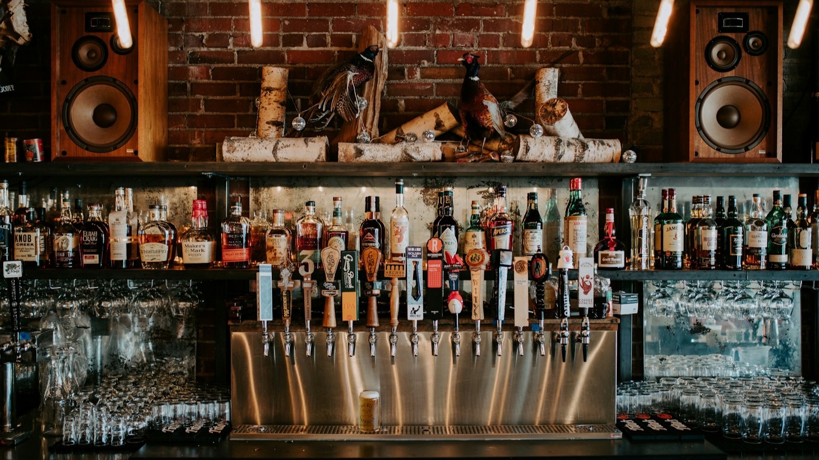A bar's back counter lined with bottles and beer taps, flanked by large speakers