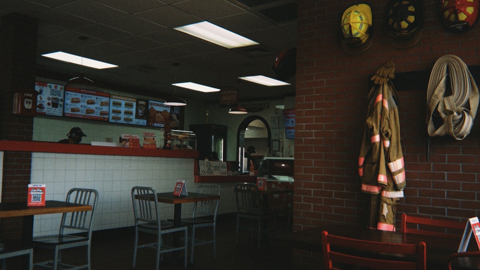 Empty sub shop dining room with firefighter helmets and gear displayed on a brick wall